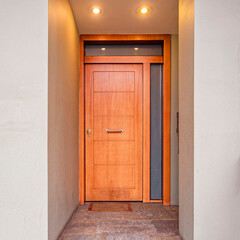 A modern house narrow entrance with a natural wooden door, Athens, Greece. Lights on.