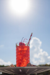 RED DRINK WITH PEPPERMINT LEAVES AND CHERRIES IN A CRYSTAL GLASS WITH CARTON STRAW ON THE SHORES OF...