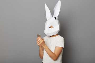 Portrait of anonymous woman wearing white t shirt and paper bunny mask, using cell phone, chatting...