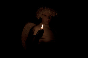 Woman angel with wings and curly hair in the dark with candles in her hands, an angel in the dark, light