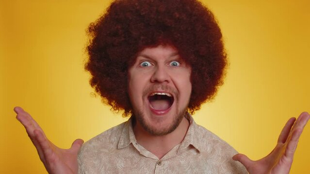 Oh my God, Wow. Excited amazed winner man with Afro hairstyle raising hands in surprise looking at camera with big eyes, shocked by sudden victory. Sincere young hipster guy boy on yellow background