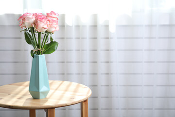 Vase with beautiful pink roses on wooden table in room. Space for text