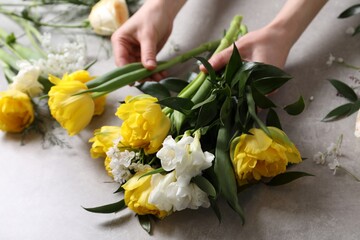Fototapeta na wymiar Florist making beautiful bouquet at grey table, closeup