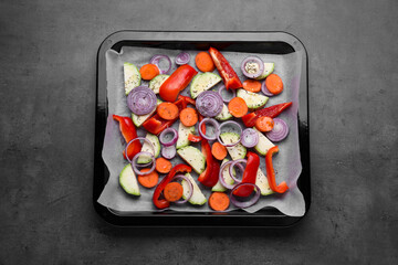 Baking pan with parchment paper and raw vegetables on dark grey table, top view