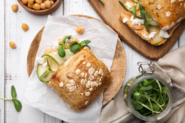 Delicious sandwiches with hummus and ingredients on white wooden table, flat lay