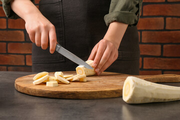 Woman cutting delicious fresh ripe parsnip at black table, closeup