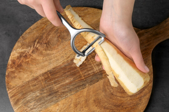 Woman Peeling Fresh Ripe Parsnip At Black Table, Above View