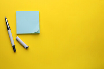 Paper note and pen on yellow background, flat lay. Space for text