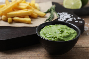 Serving board with french fries, avocado dip, rosemary and lime served on wooden table, closeup