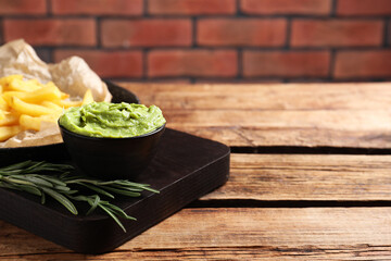 Serving board with parchment, french fries, avocado dip and rosemary on wooden table, space for text