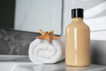 Bottle of shower gel and rolled towel with starfish on sink in bathroom