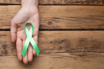World Mental Health Day. Woman holding green ribbon on wooden background, top view with space for...