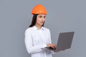 Serious woman in protective helmet with laptop computer isolated on grey background. Young woman construction manager. Architect woman, female worker in hardhat helmet.