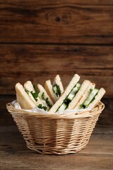 Tasty sandwiches with cucumber and parsley in wicker basket on wooden table