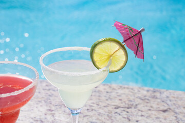 MARGARITAS. CHERRY AND LEMON DAISIES ON THE EDGE OF A POOL ON A SUNNY DAY