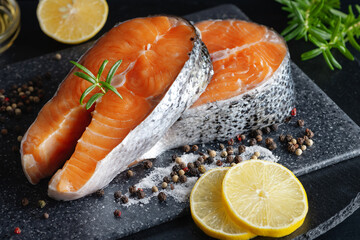 Delicious fresh salmon with lemon, salt and spices on a black table. Concept of healthy seafood