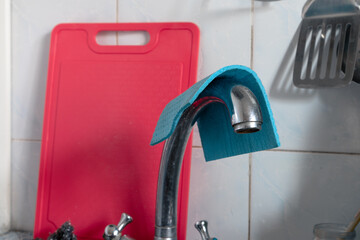 Water faucet with a rag on top and a red cutting board in the background