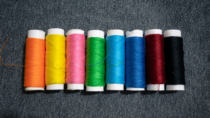 Spools with multi-colored threads on a gray fabric. Panoramic image of colorful threads
