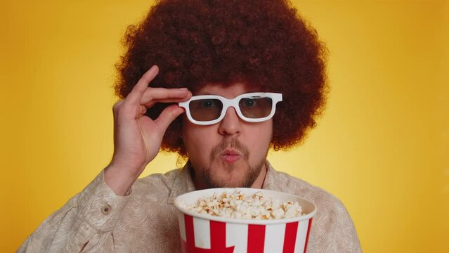Excited bearded man with afro hairstyle eating popcorn and watching interesting tv serial, sport game, online social media movie film content. Hipster guy in 3D glasses enjoying domestic entertainment