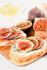 Toast with fresh fig, cream cheese and prosciutto on wooden cutting board. Healthy quick breakfast recipe. Vertical image. Selective focus