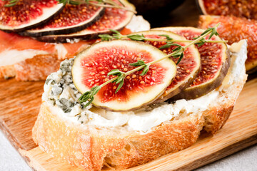 Toast with raw ripe fig, blue cheese and herbs on wooden cutting board. Healthy quick breakfast idea. Italian cuisine. Selective focus