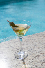 COLD MARTINI GLASS WITH OLIVES ON THE SHORES OF A POOL ON A SUNNY DAY