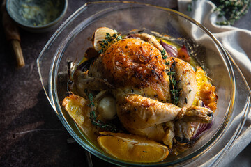 Oven roasted coquelet jaune (yellow spring chicken) with oranges, onions and herb butter in glass baking dish.