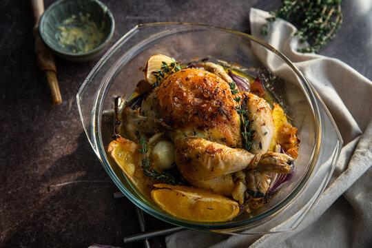 Oven roasted coquelet jaune (yellow spring chicken) with oranges, onions and herb butter in glass baking dish.