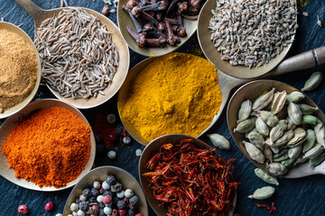 Fototapeta na wymiar Set of spices in brass spoons, closeup, top view. Various peppers, cardamom, carnation, turmeric, paprika and saffron for cooking