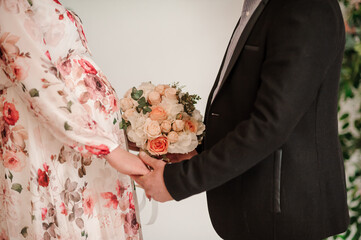 The groom holds the bride's hand, in the background a wedding bouquet with multi-colored flowers