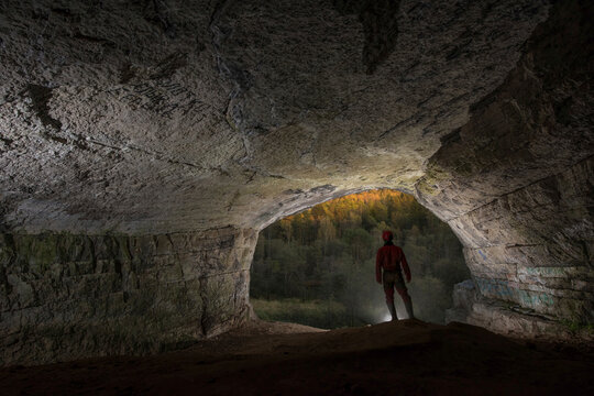 Shortly before sunset, a man stands looking out at a forest at the entrance to Ignatievskaya cave in the Ural Mountains; Russia
