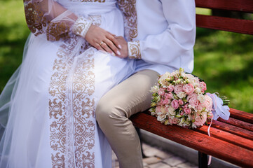 The groom holds the bride's hand, in the background a wedding bouquet with multi-colored flowers