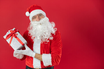 Portrait von einem verkleideten Weihnachtsmann mit Geschenk, isoliert auf roten Hintergrund im...