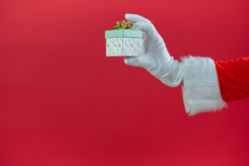 Nahaufnahme von der Hand von einem Weihnachtsmann, der ein Geschenk, vor roten Hintergrund, hält....