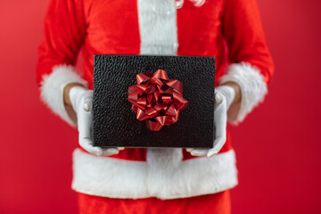 Nahaufnahme von der Hand von einem Weihnachtsmann, der ein Geschenk, vor roten Hintergrund, hält....