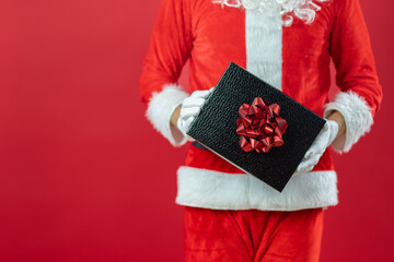 Nahaufnahme von der Hand von einem Weihnachtsmann, der ein Geschenk, vor roten Hintergrund, hält. Weihnachtlicher Hintergrund mit Platzhalter.