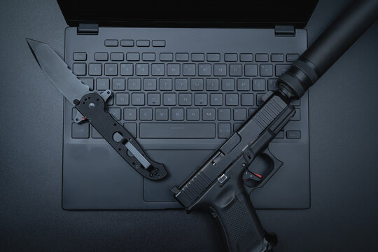 Tactical weapon and computer.  A pistol with a silencer, a folding knife and a laptop, close-up photo.