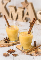 Two glasses of eggnogg with cinnamon sticks on white wooden background, christmas. Auld Man's milk, Coquito or Creme de Vie or Eierlikör. Vertical.