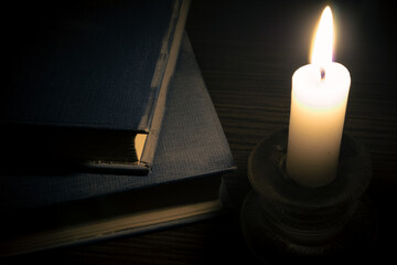 Old books and a burning candle on the table in the dark