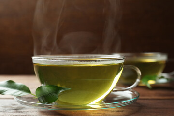 Fresh green tea in glass cup with saucer and leaves on wooden table, closeup