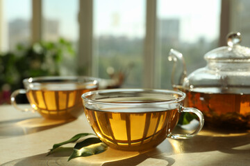 Fresh green tea in glass cups, leaves and teapot on table indoors