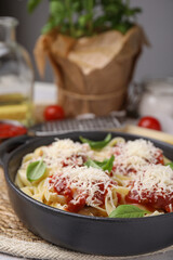 Delicious pasta with tomato sauce, basil and parmesan cheese on wicker mat, closeup