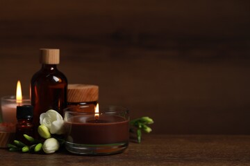 Beautiful spa composition with burning candles, different care products and flowers on wooden table. Space for text