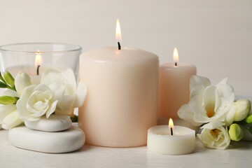 Fototapeta na wymiar Beautiful composition with burning candles, spa stones and flowers on white table, closeup