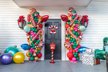 A white siding building exterior with a black door and colums of balloons and large ornaments and...