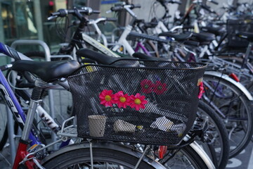 Fototapeta na wymiar Bicycle with black metal wire basket decorated with red plastic flowers. In the basket there are empty paper coffee cups. A detail of crowded bicycle in parking lot.