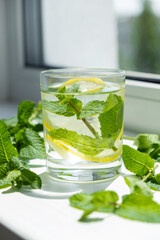 Detox water with mint and lemon on window sill and fresh mint leaves around. Herbal vitamin drink. Summer refreshing drink.