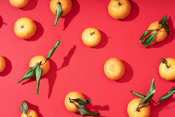 Fresh ripe small tangerines with leaves lie on a wooden plate. Red festive fruit background. Happy Chinese New Year 2023 concept.