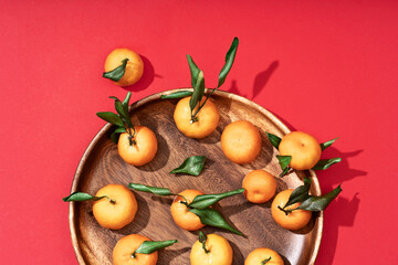 Fresh ripe small tangerines with leaves lie on a wooden plate. Red festive fruit background. Happy Chinese New Year 2023 concept.