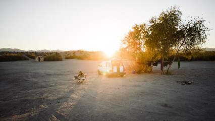 Aerial view drone shot of van life living and working in remote area of nevada usa desert with sun setting in distance with warm orange hues and bright over exposed sky for copy space.